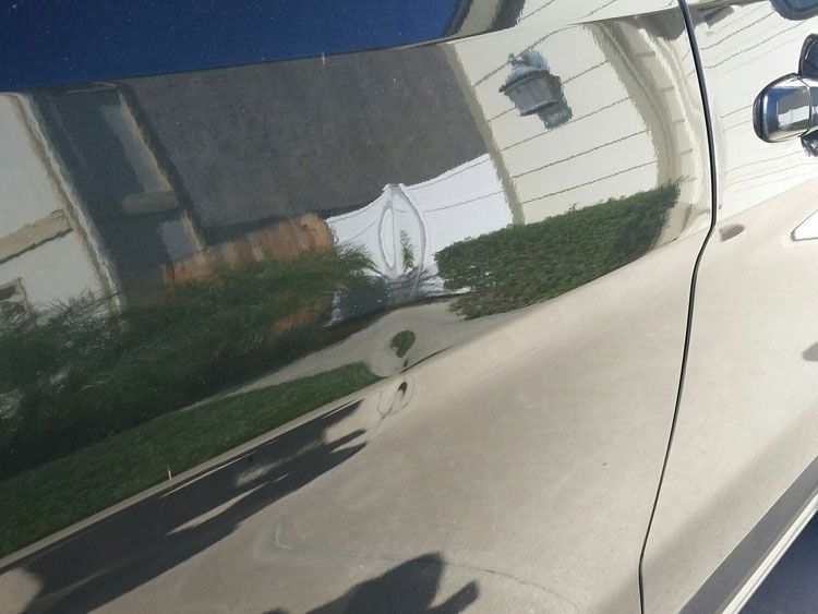 A car door with a reflection of a house in it