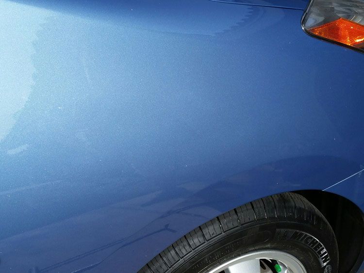 A close up of a blue car 's fender and tire