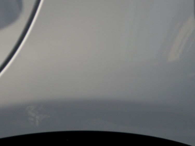A close up of a silver car fender with a black tire.