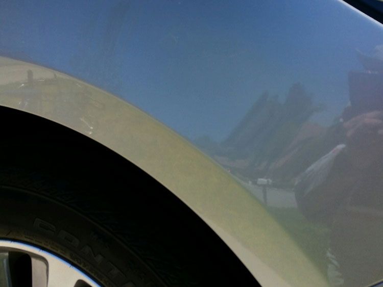 A close up of a car fender with a blue sky in the background