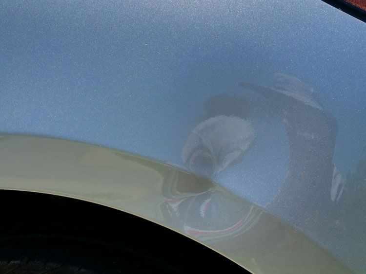 A close up of a car fender with a reflection of a car in it.
