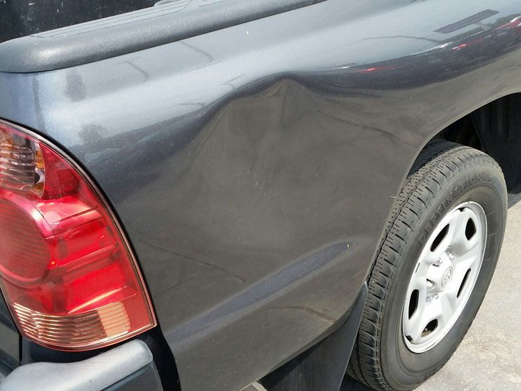 A black truck with a damaged fender is parked on the side of the road