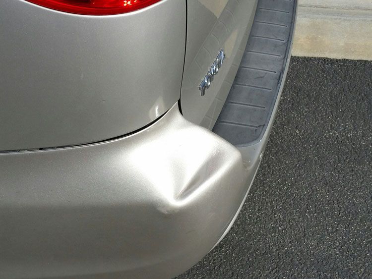 A silver van with a damaged bumper is parked on the street