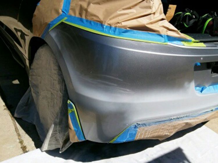 A bumper of a car is taped with blue tape