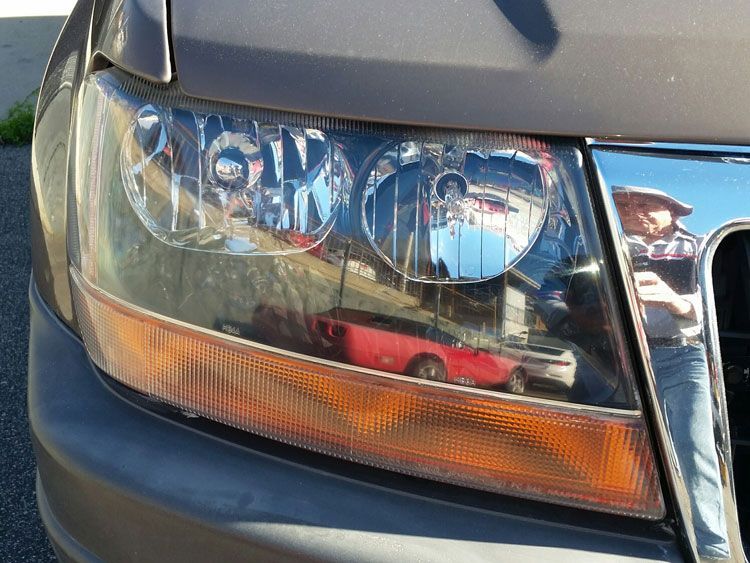 A close up of a car headlight with a red truck in the background