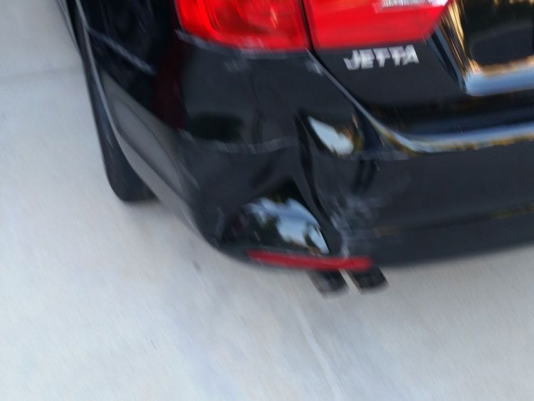 A black car with a damaged bumper is parked in a driveway