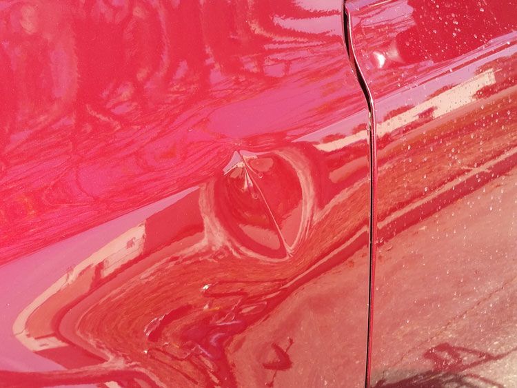 A close up of a red car with a damaged door.
