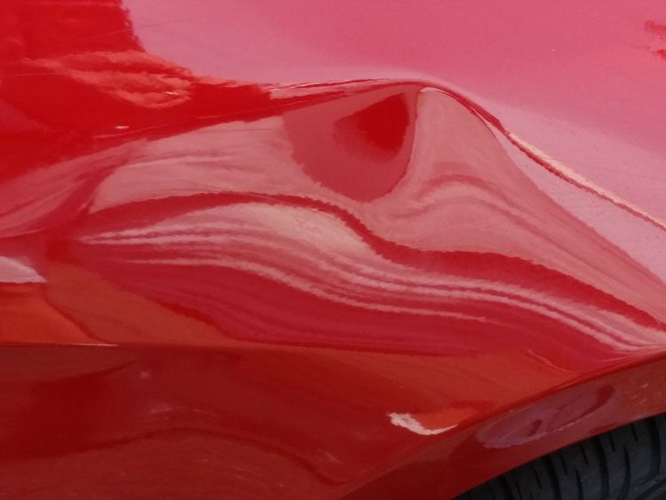 A close up of a red car with a dent in the fender.