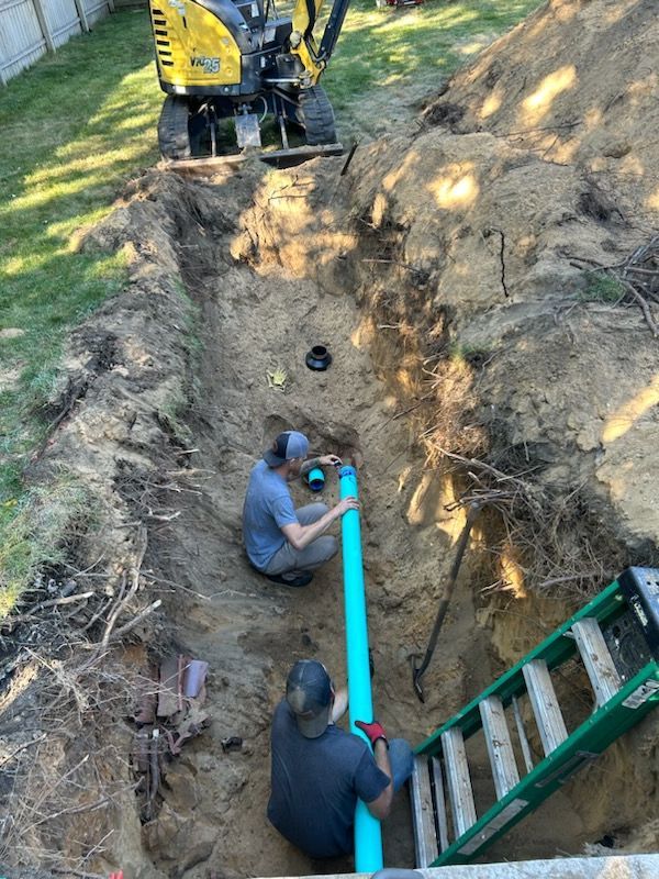 Two men are working on a pipe in a trench.