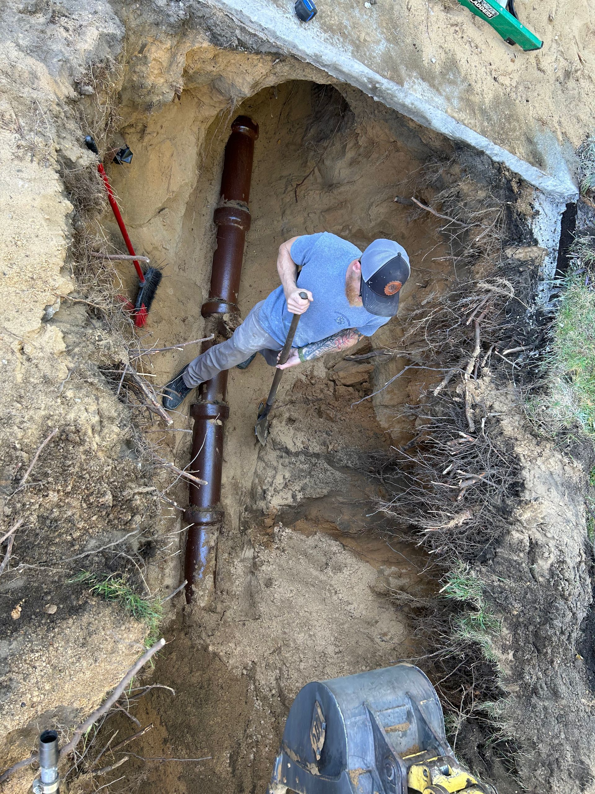 A man is digging a hole in the ground next to a pipe.