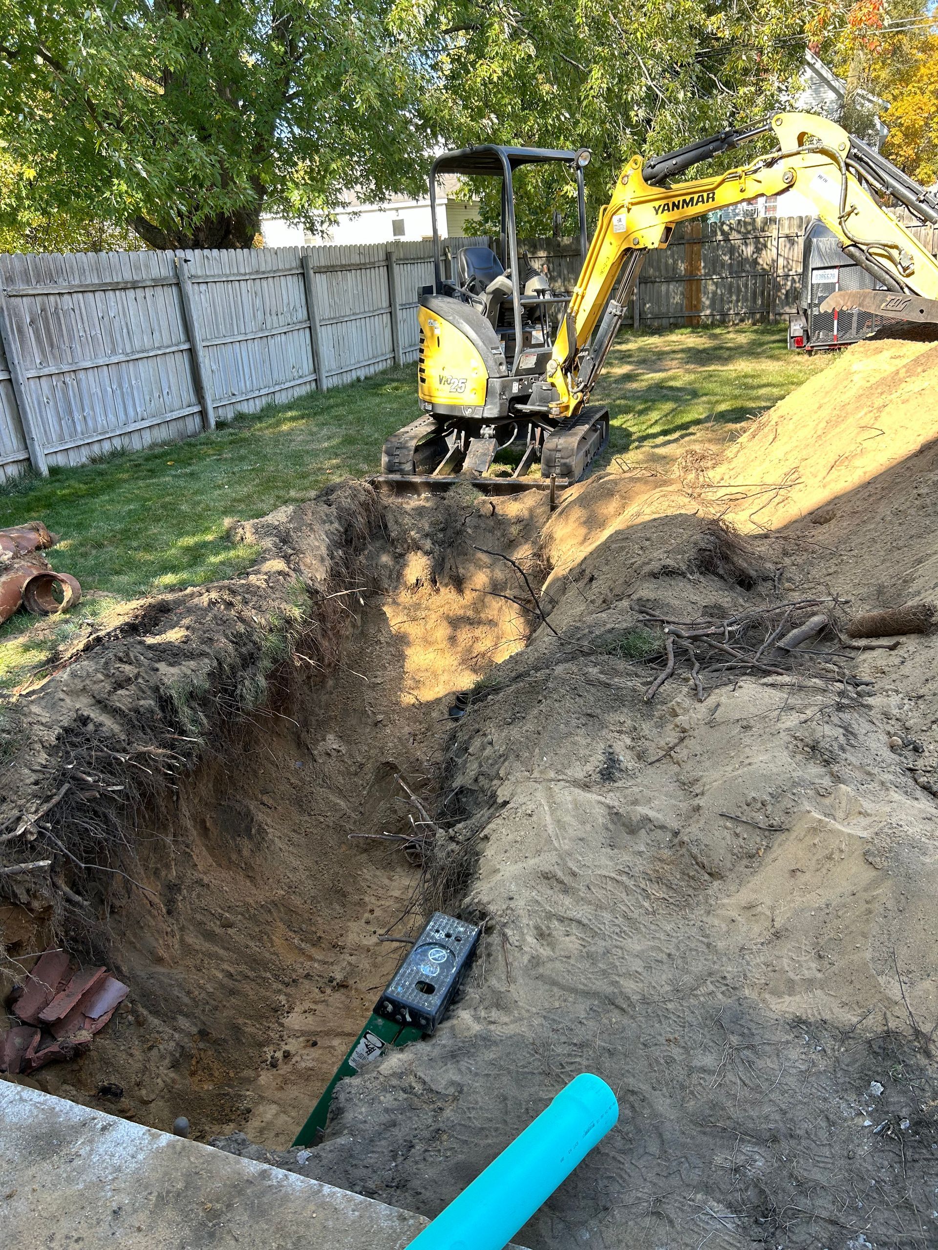 A yellow excavator is digging a hole in the dirt in a backyard.