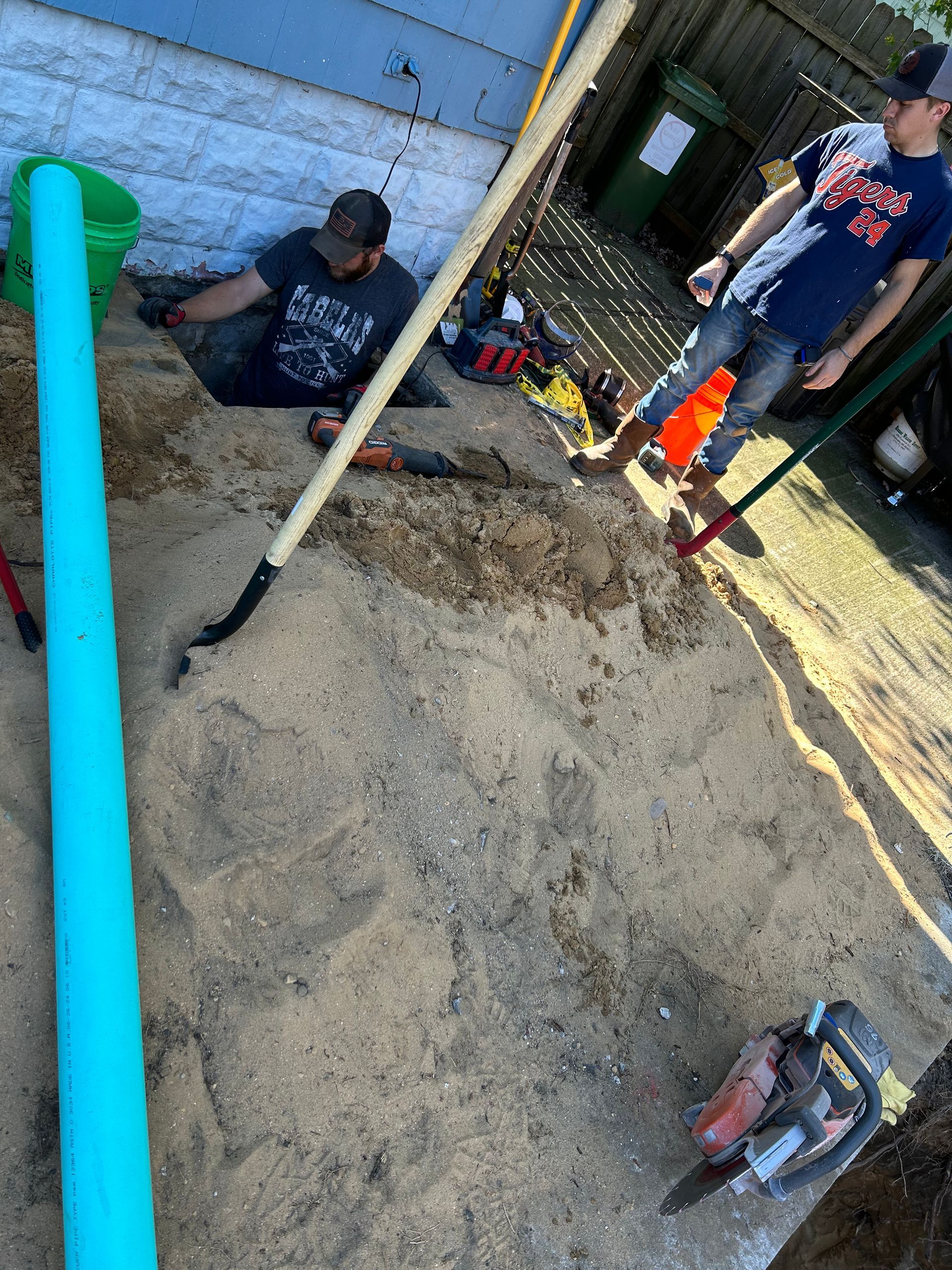 A man is laying in the dirt next to a blue pipe.