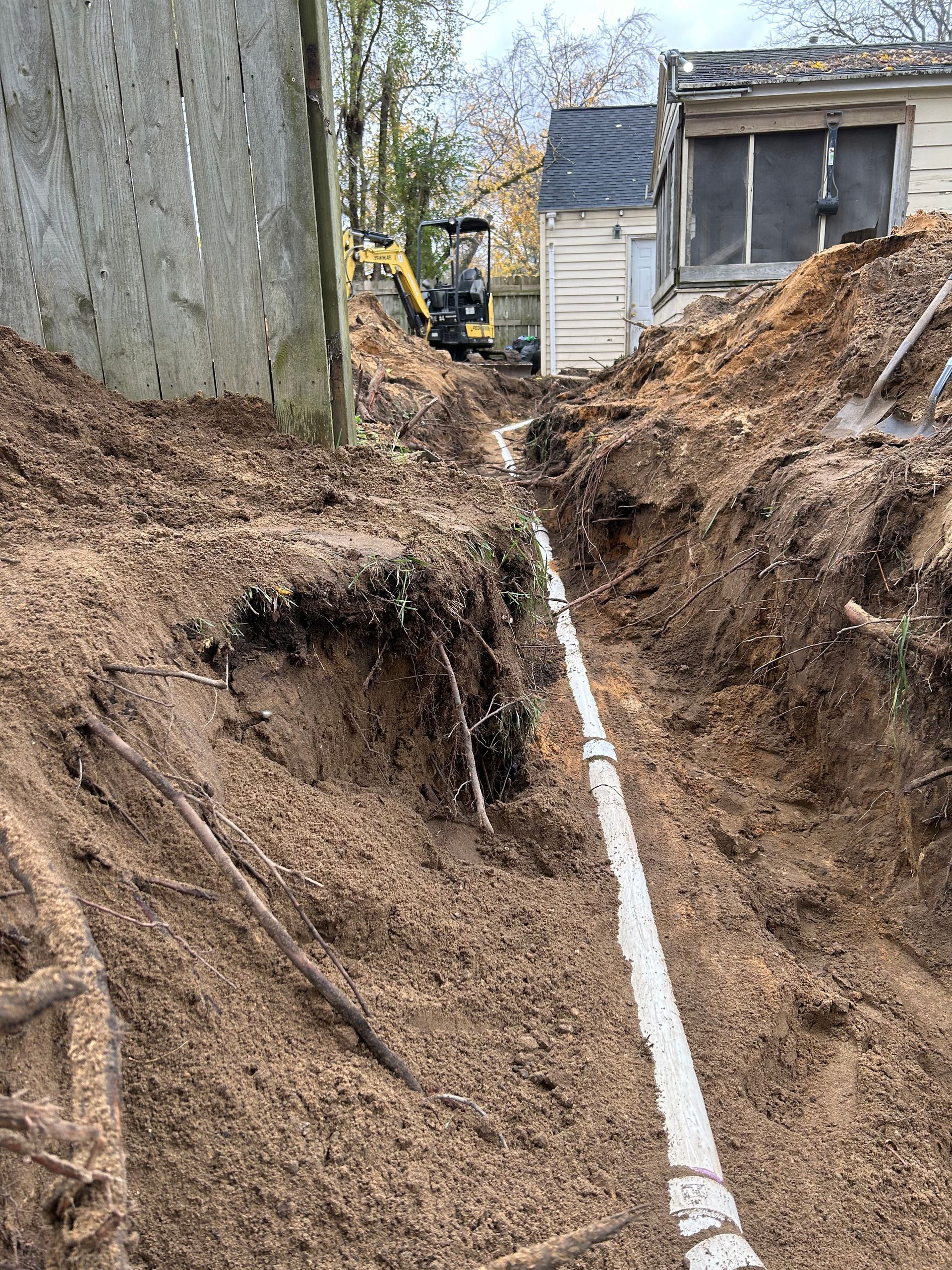 A drain pipe is being installed in the dirt next to a house.