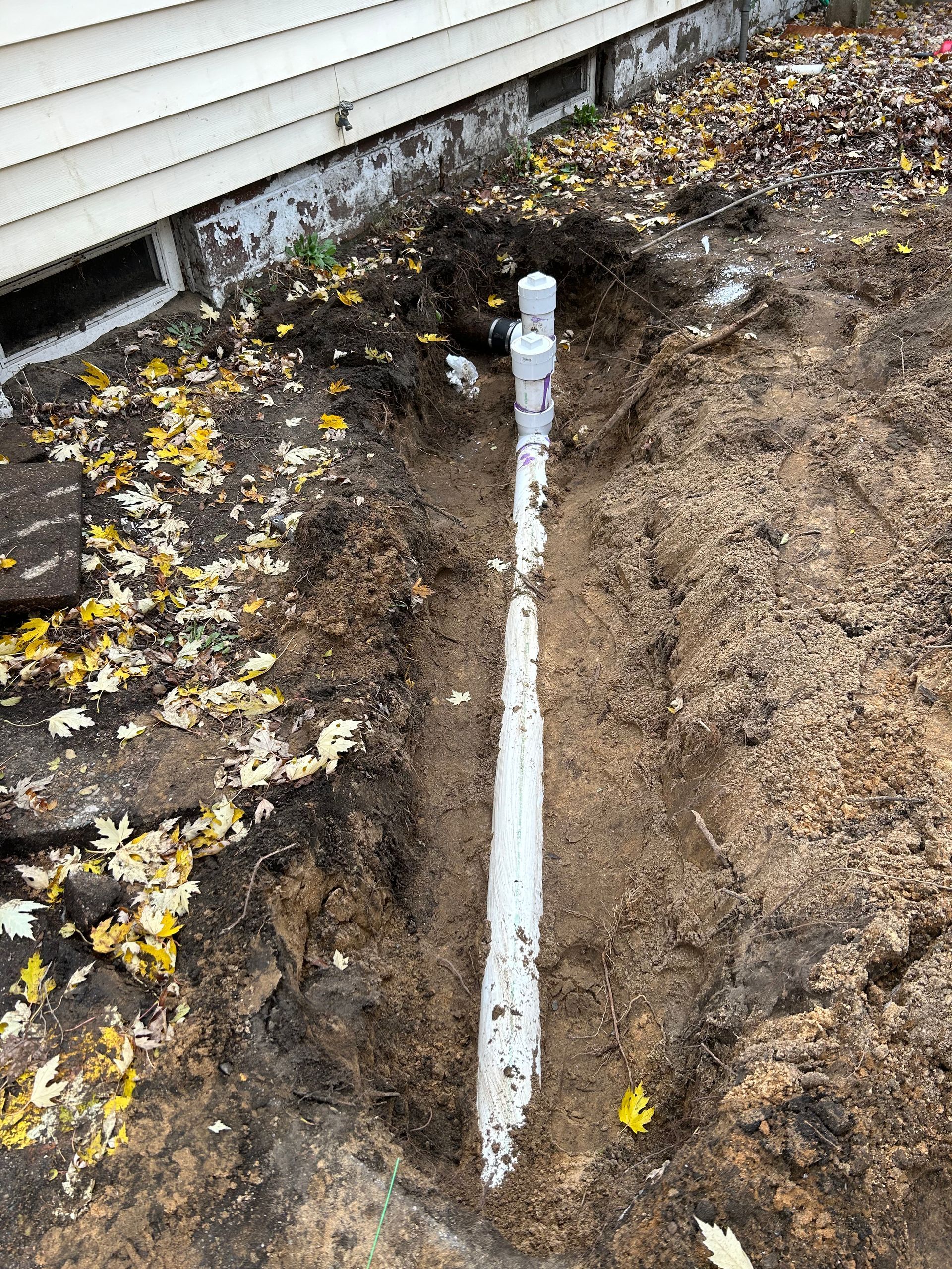 A white pipe is sitting in the dirt next to a house.