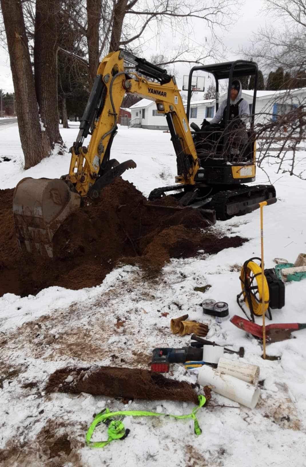 A yellow excavator is digging a hole in the snow.