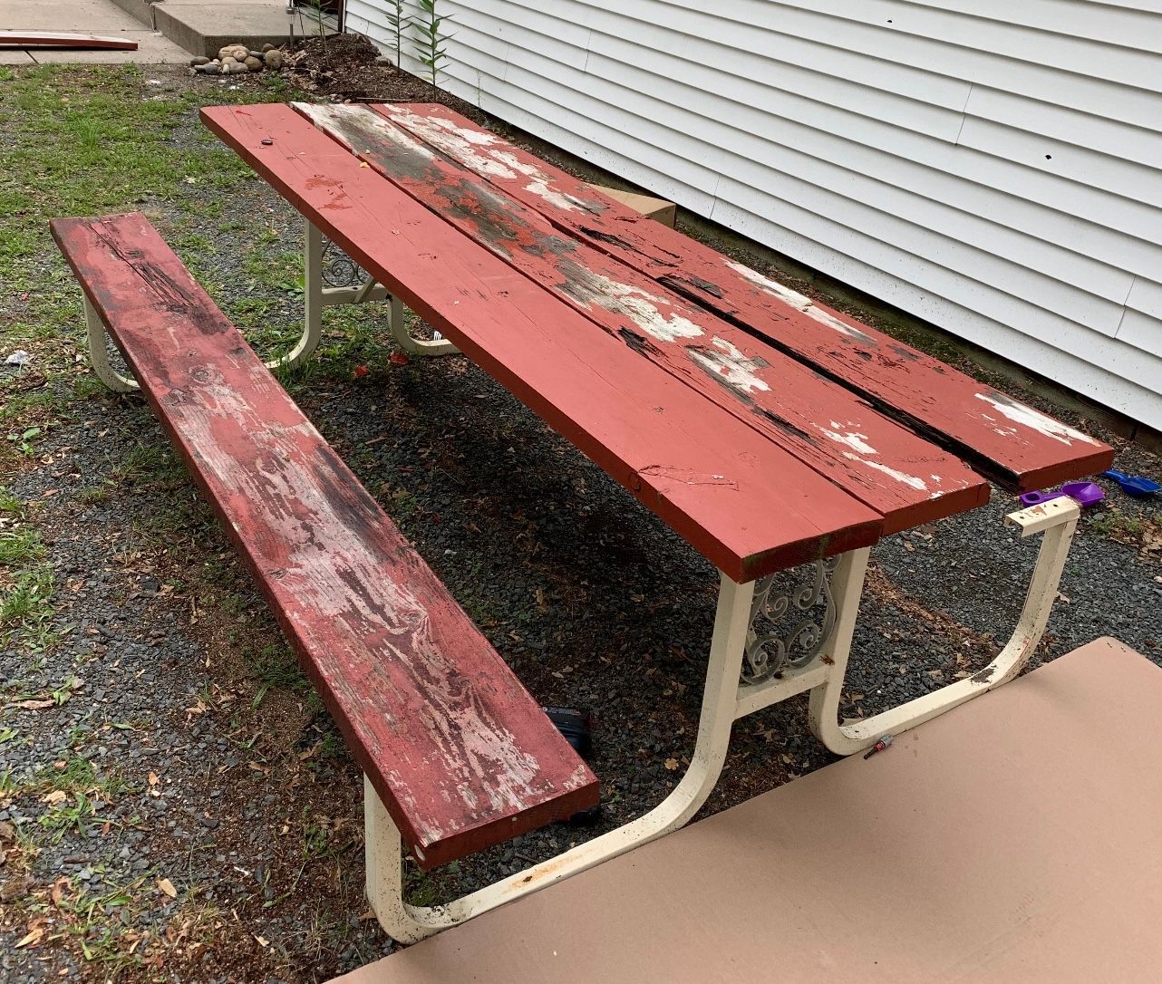 A red picnic table is sitting in front of a white house.