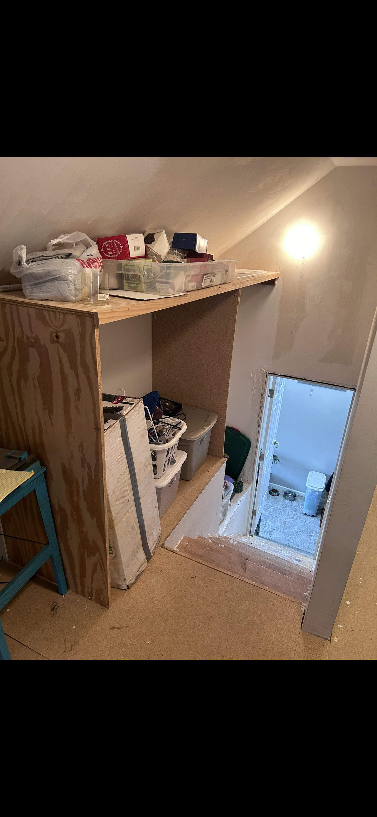 A room with a shelf and stairs leading to a bathroom.