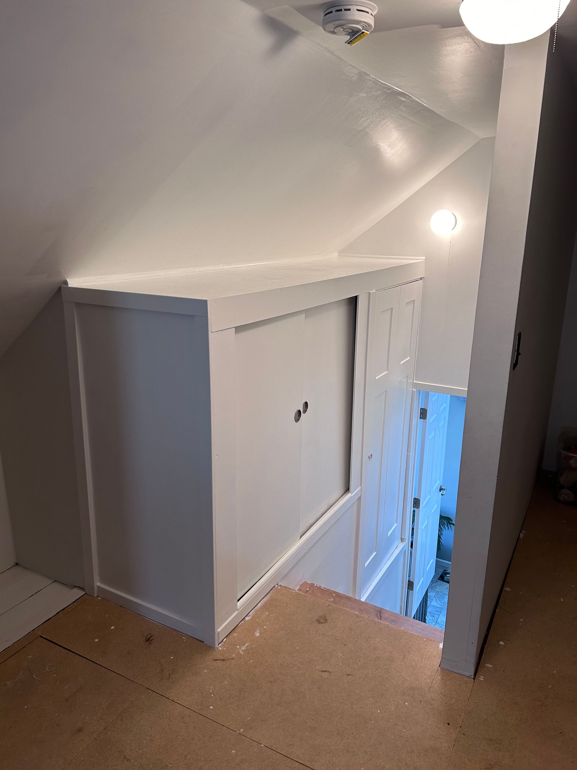 A room with a staircase and a closet in the corner.