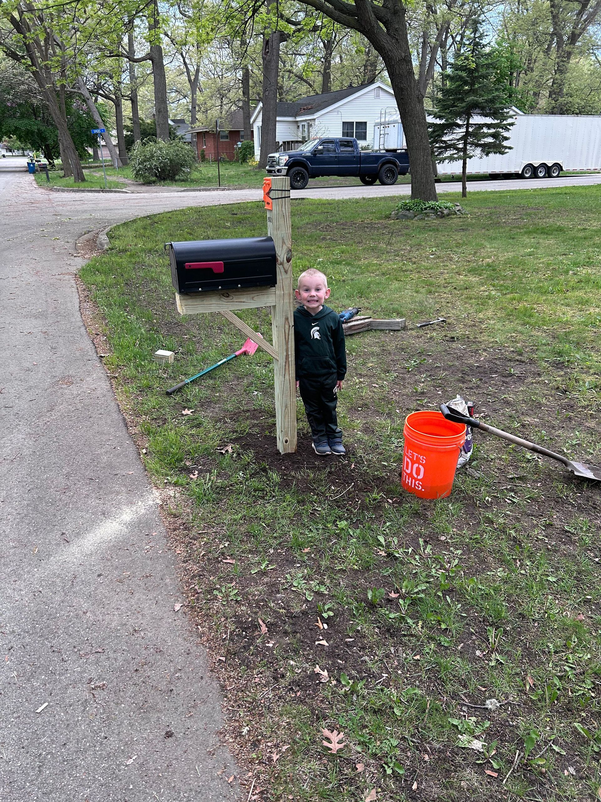 A little boy is standing next to a wooden post in a yard.