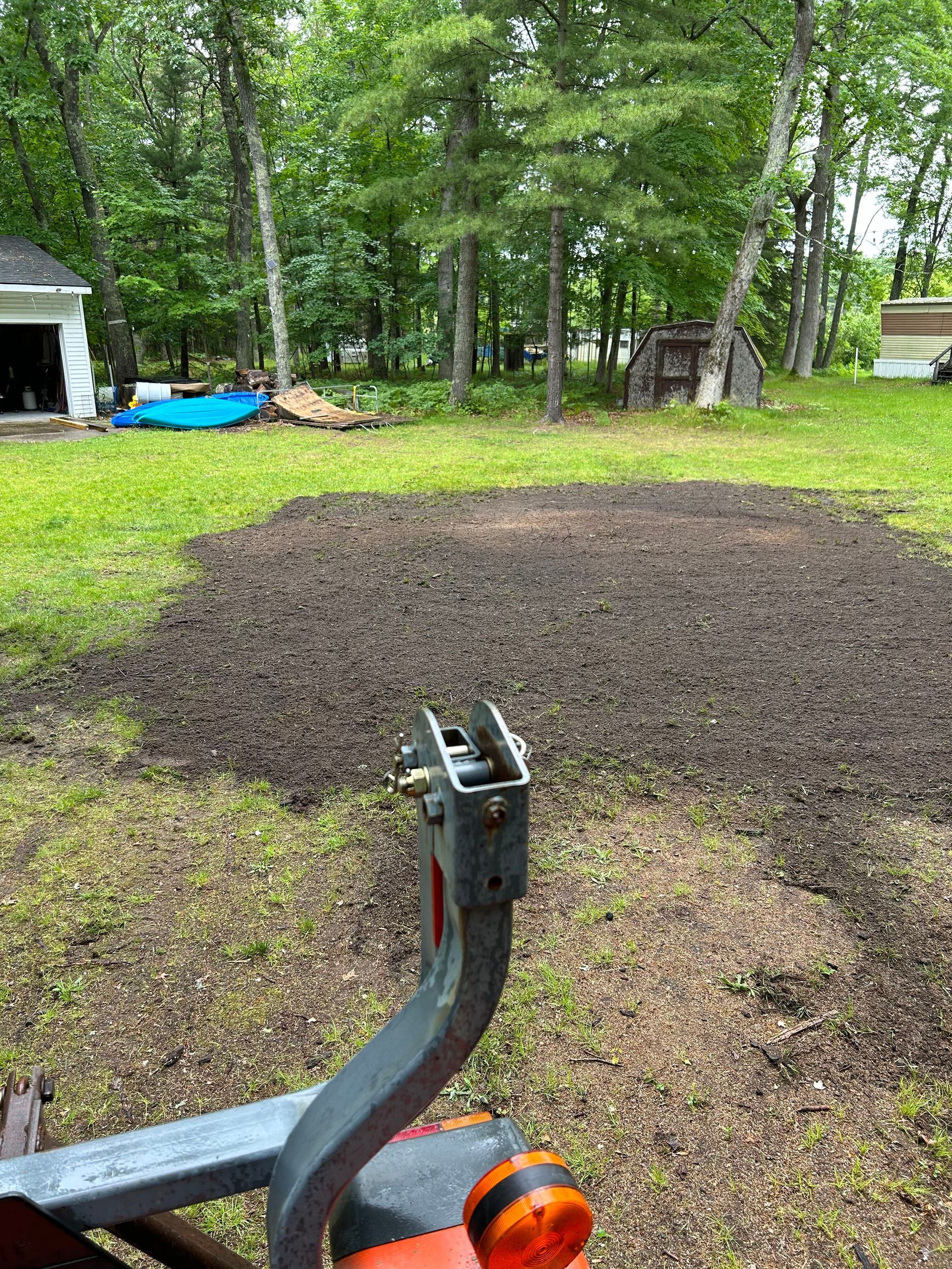 A tractor is plowing a large area of dirt in a backyard.