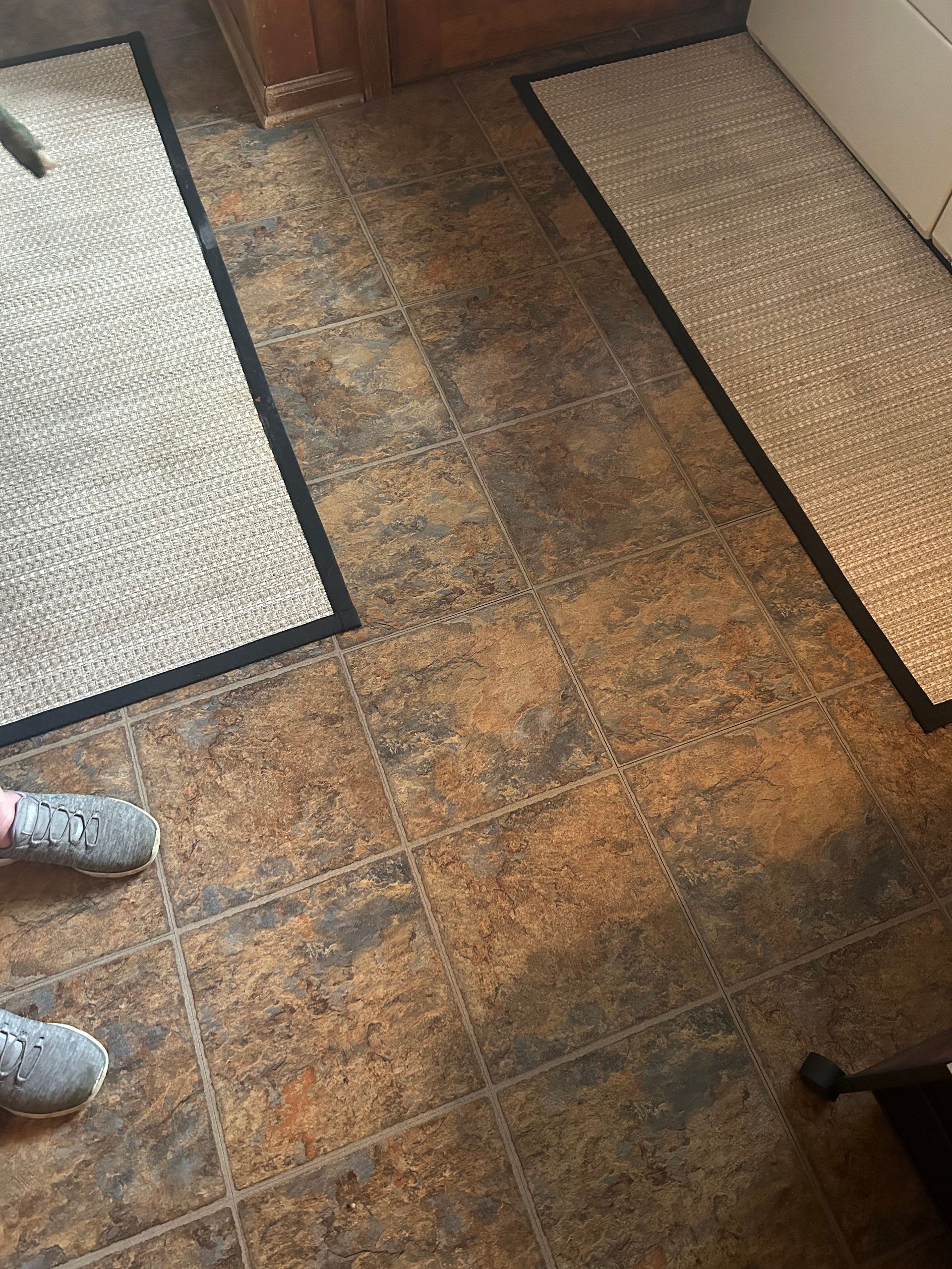 A person is standing on a tiled floor next to a rug.