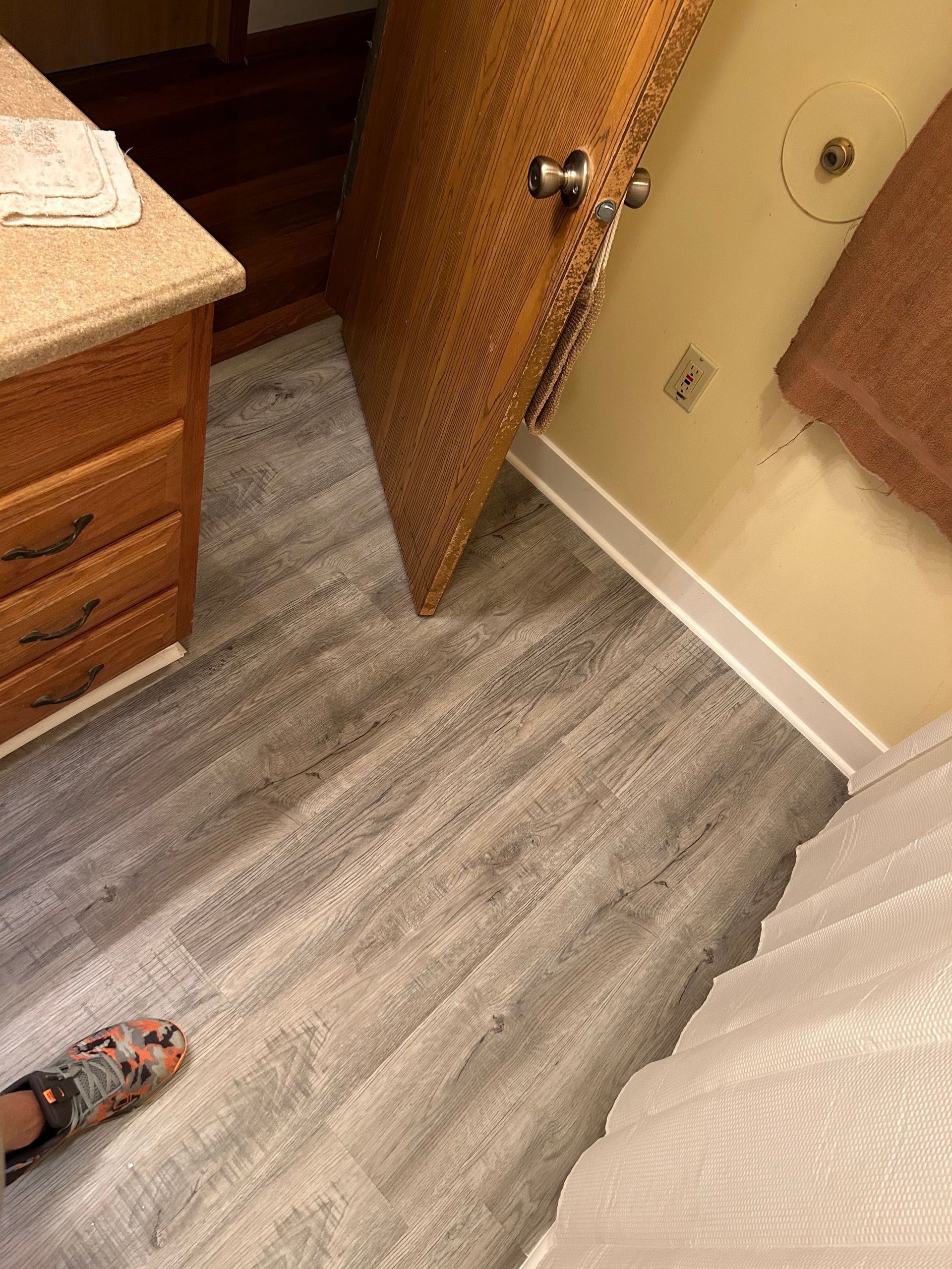 A person is standing on a wooden floor in a bathroom.