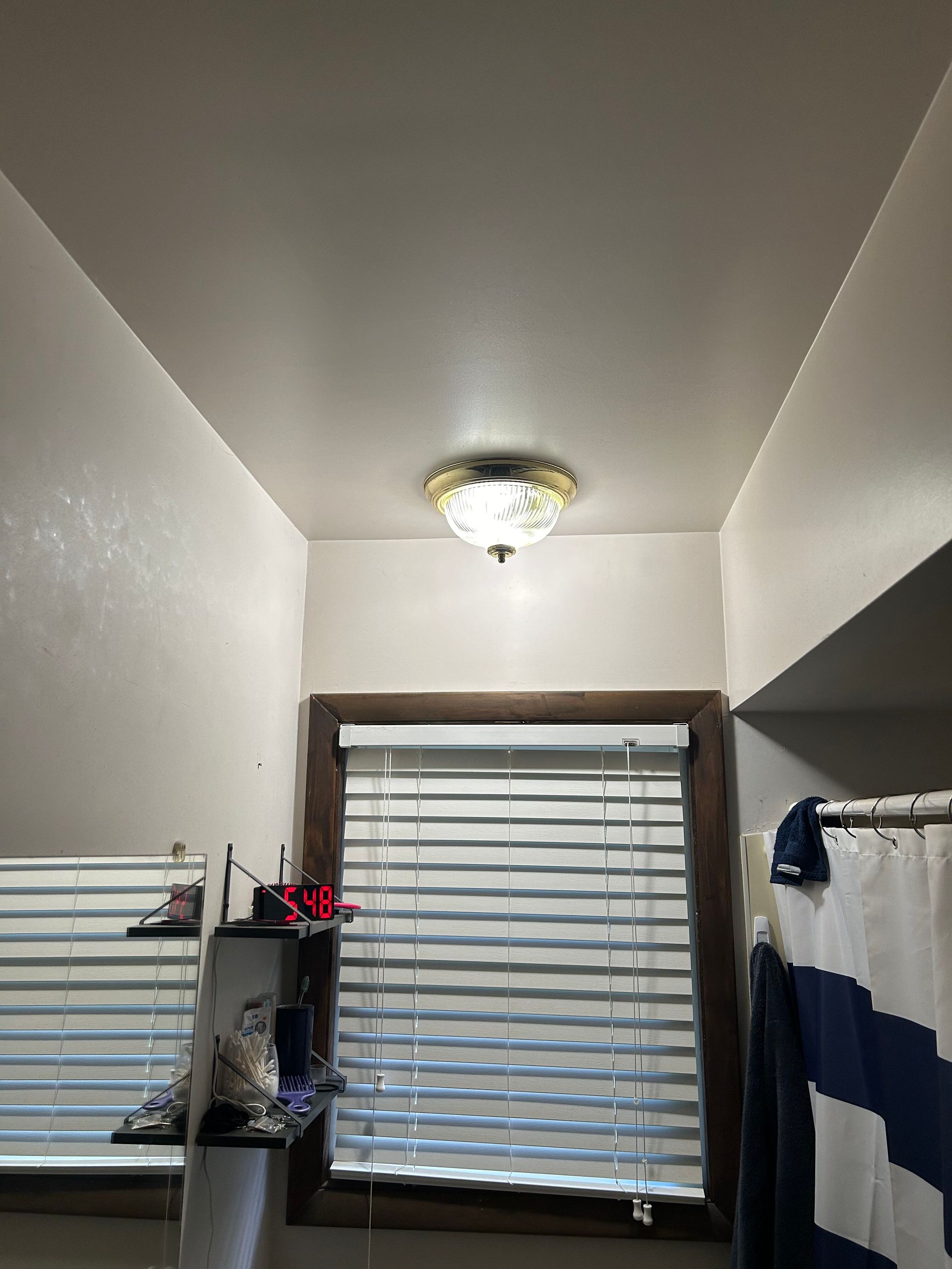 A bathroom with a shower curtain and a window with blinds.