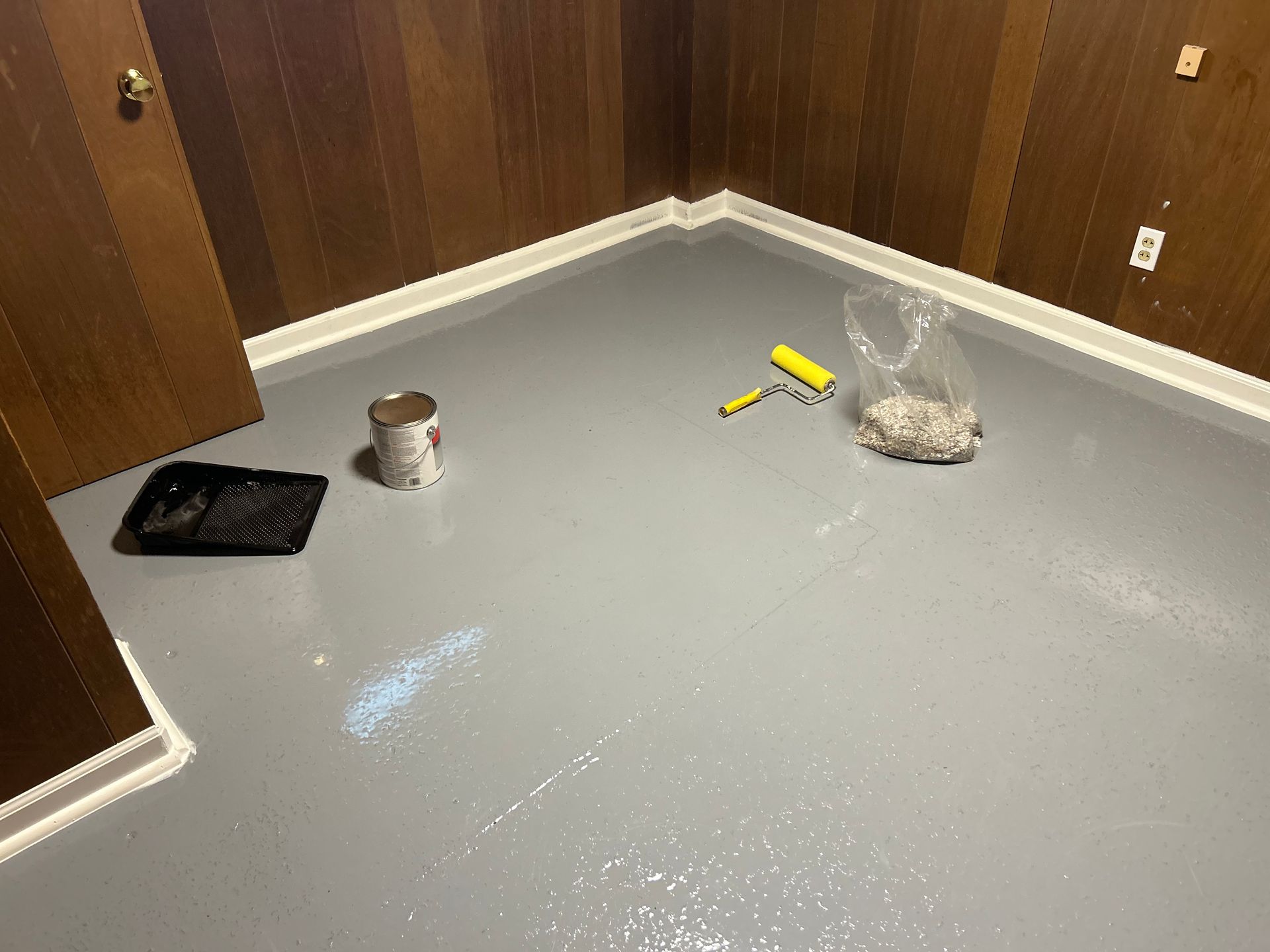 A room with a gray floor and wooden walls is being painted.