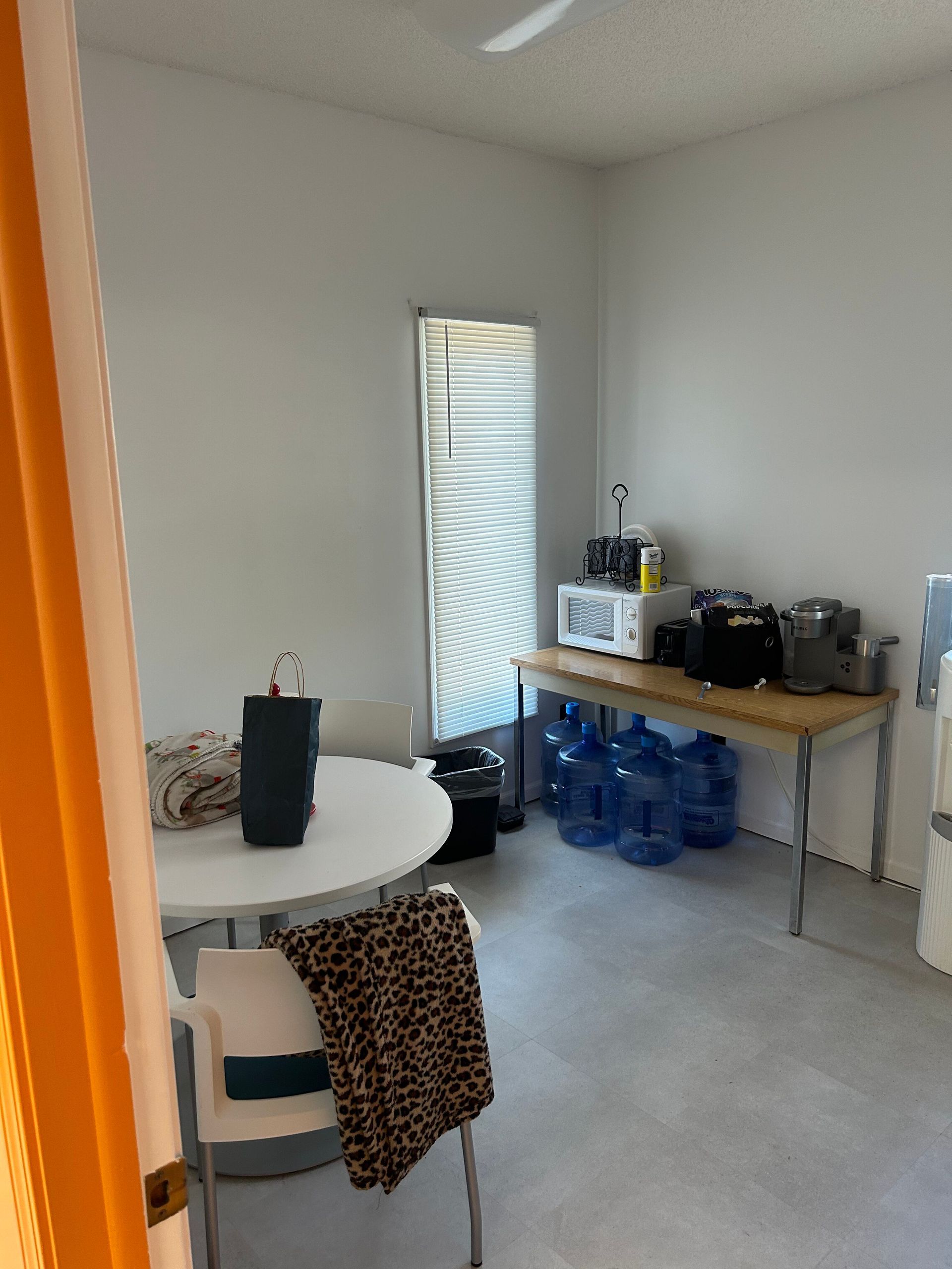 A room with a table , chairs , water bottles and a microwave.