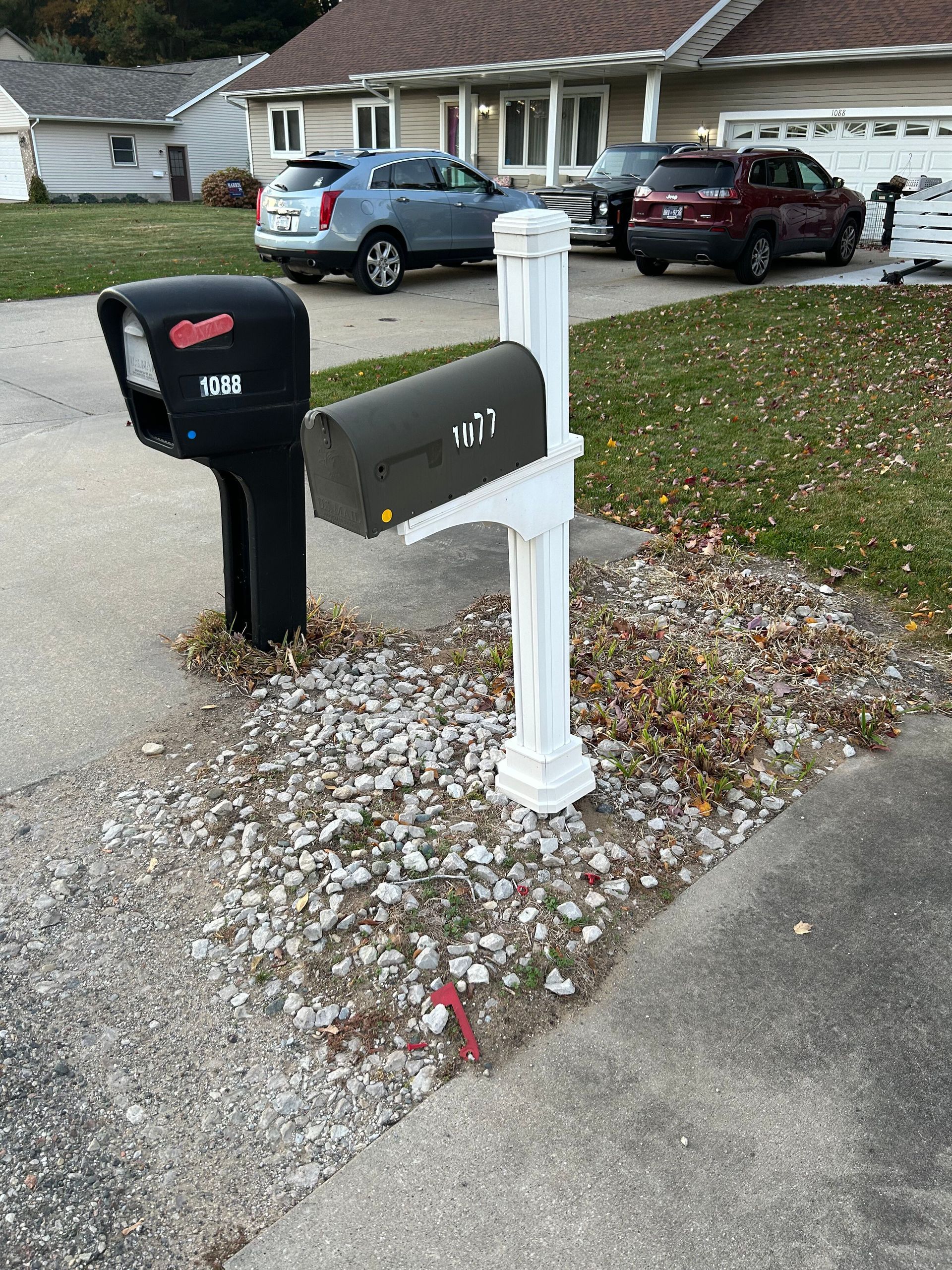 A black mailbox is next to a white mailbox in front of a house.