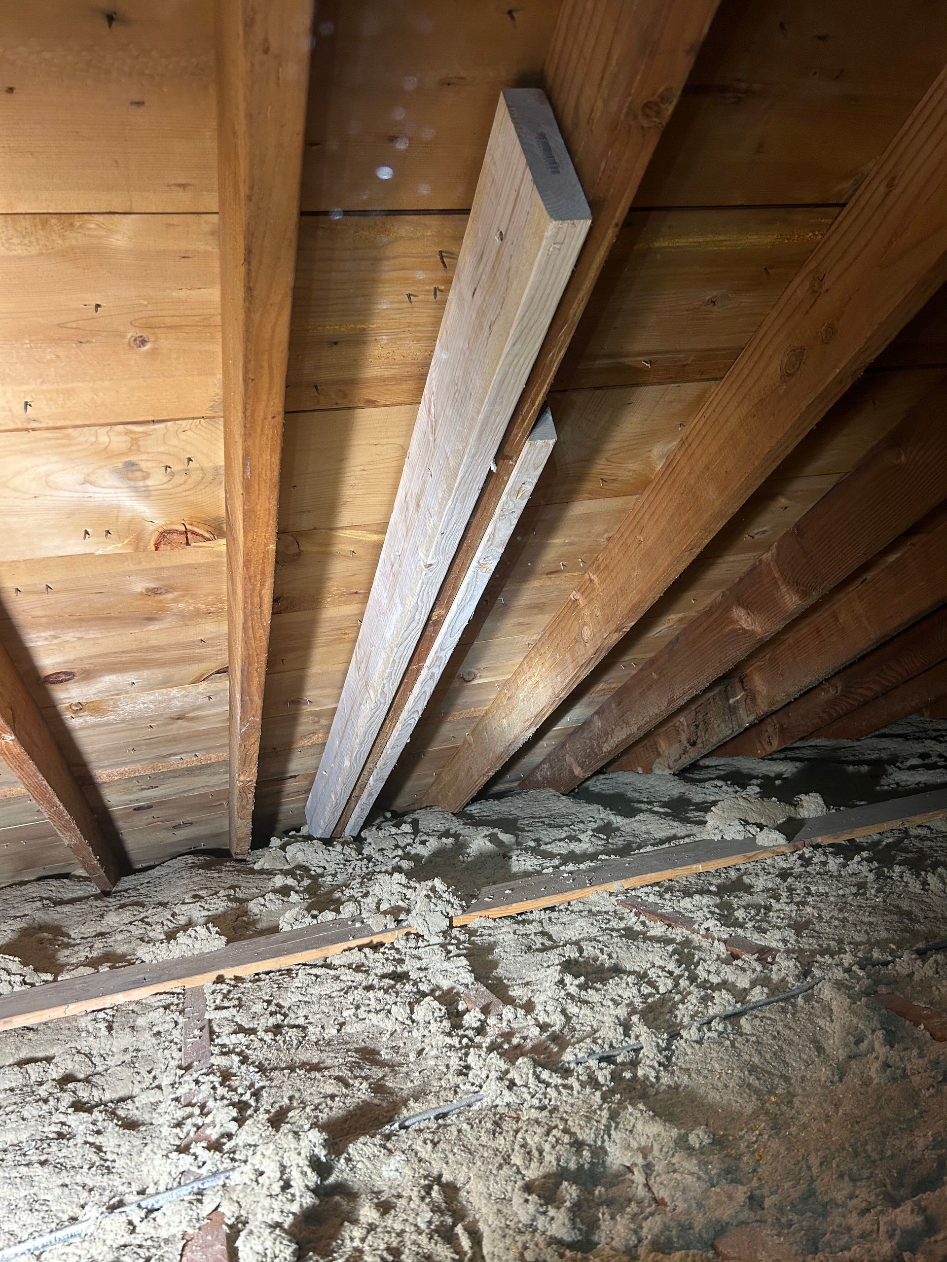 A wooden beam is hanging from the ceiling of an attic.