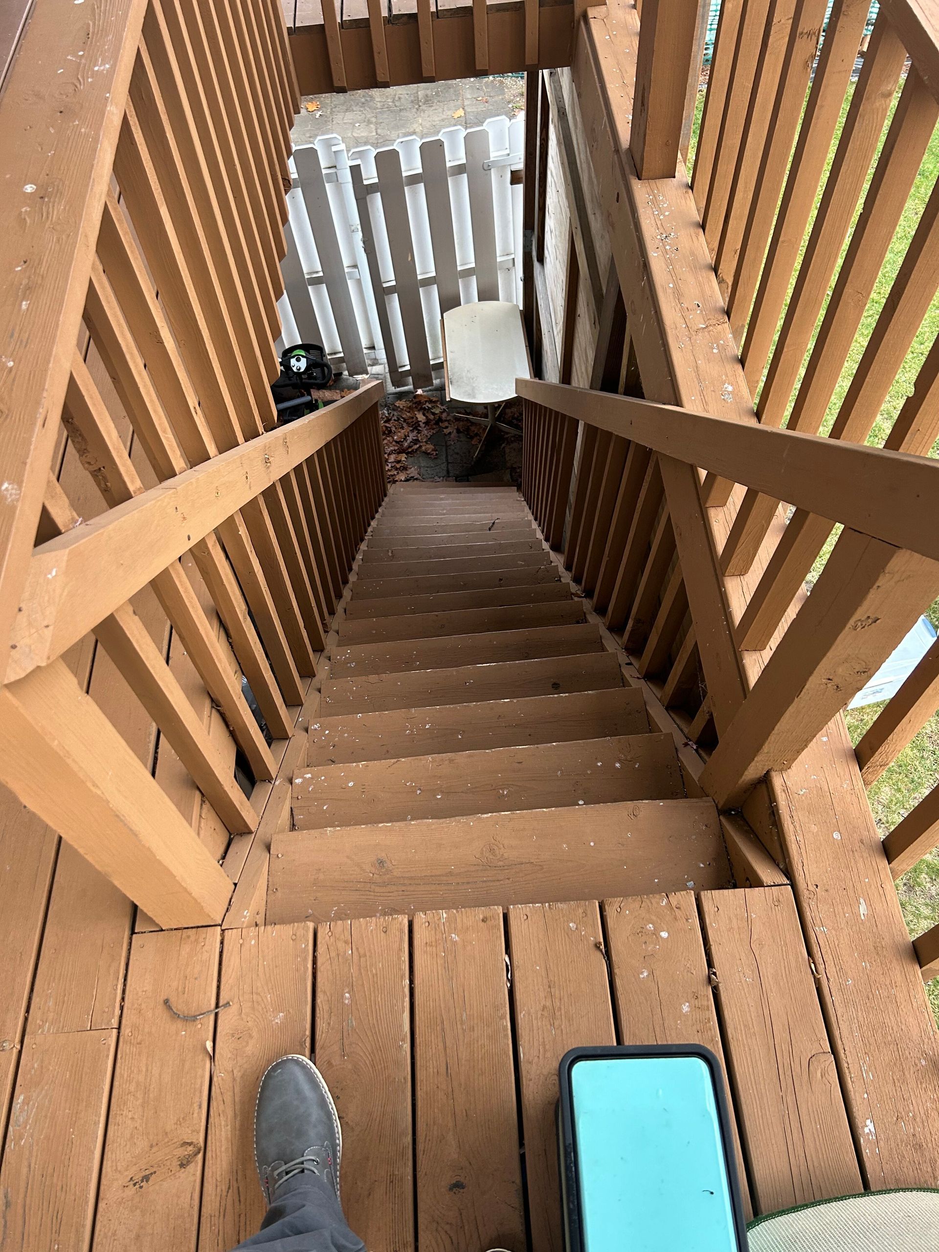 A person is standing on a wooden deck looking down a set of stairs.
