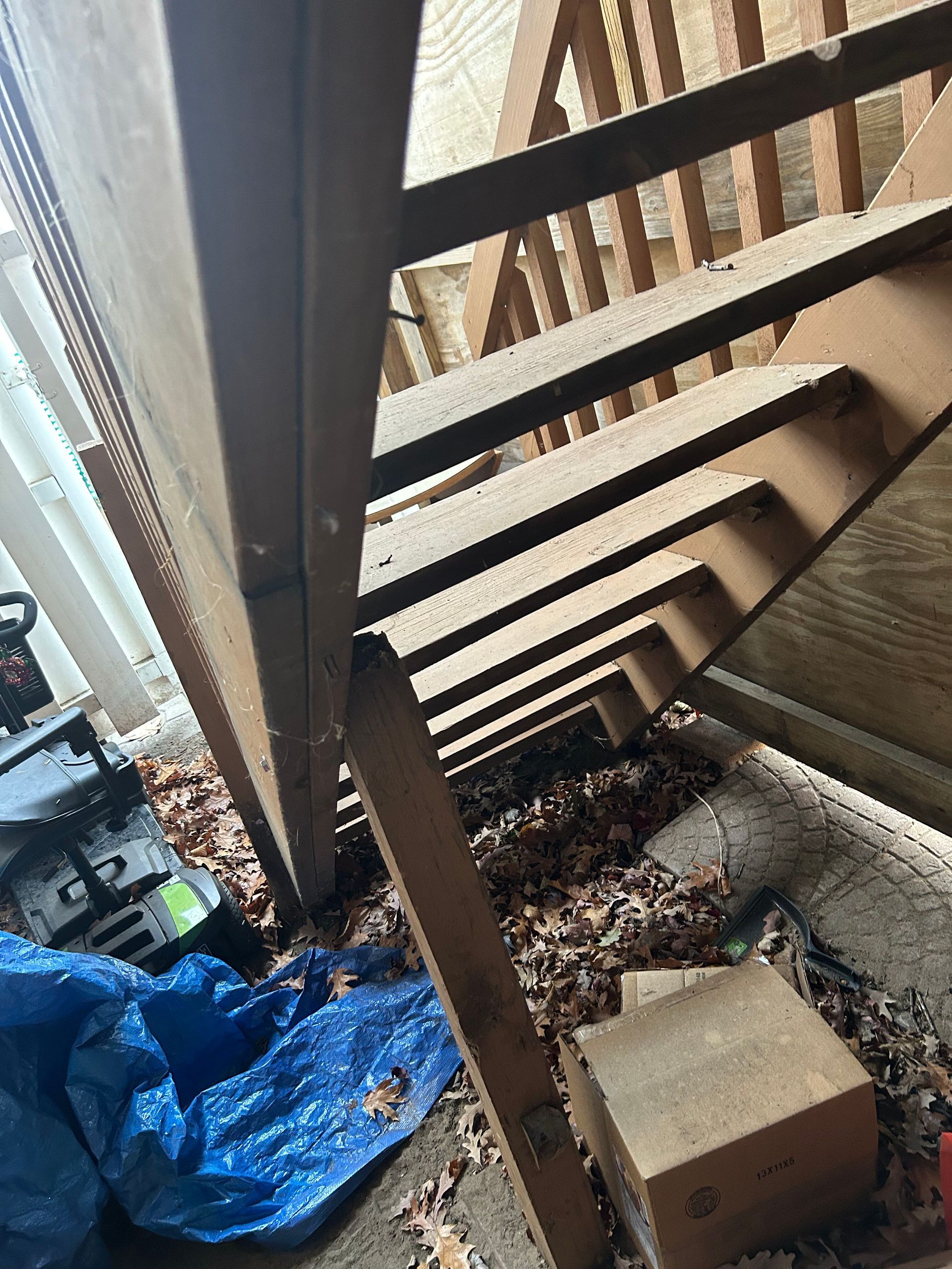 A wooden staircase with a blue tarp on the ground underneath it