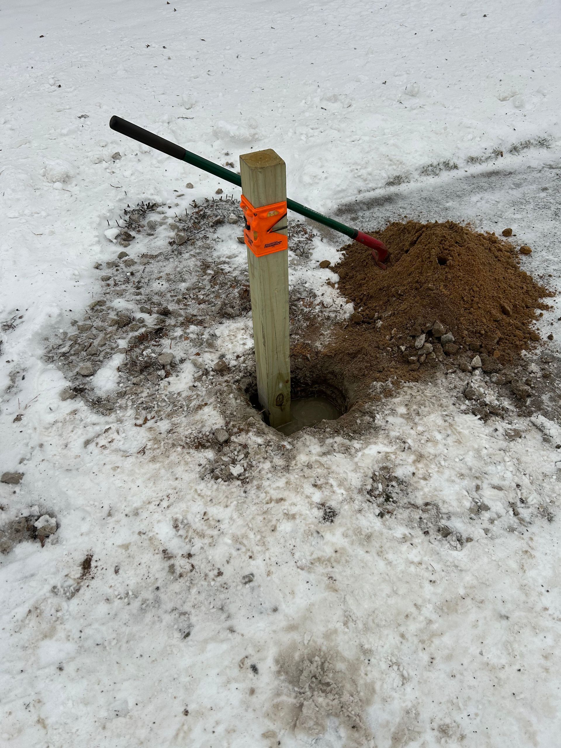 A wooden post is sticking out of a hole in the snow.