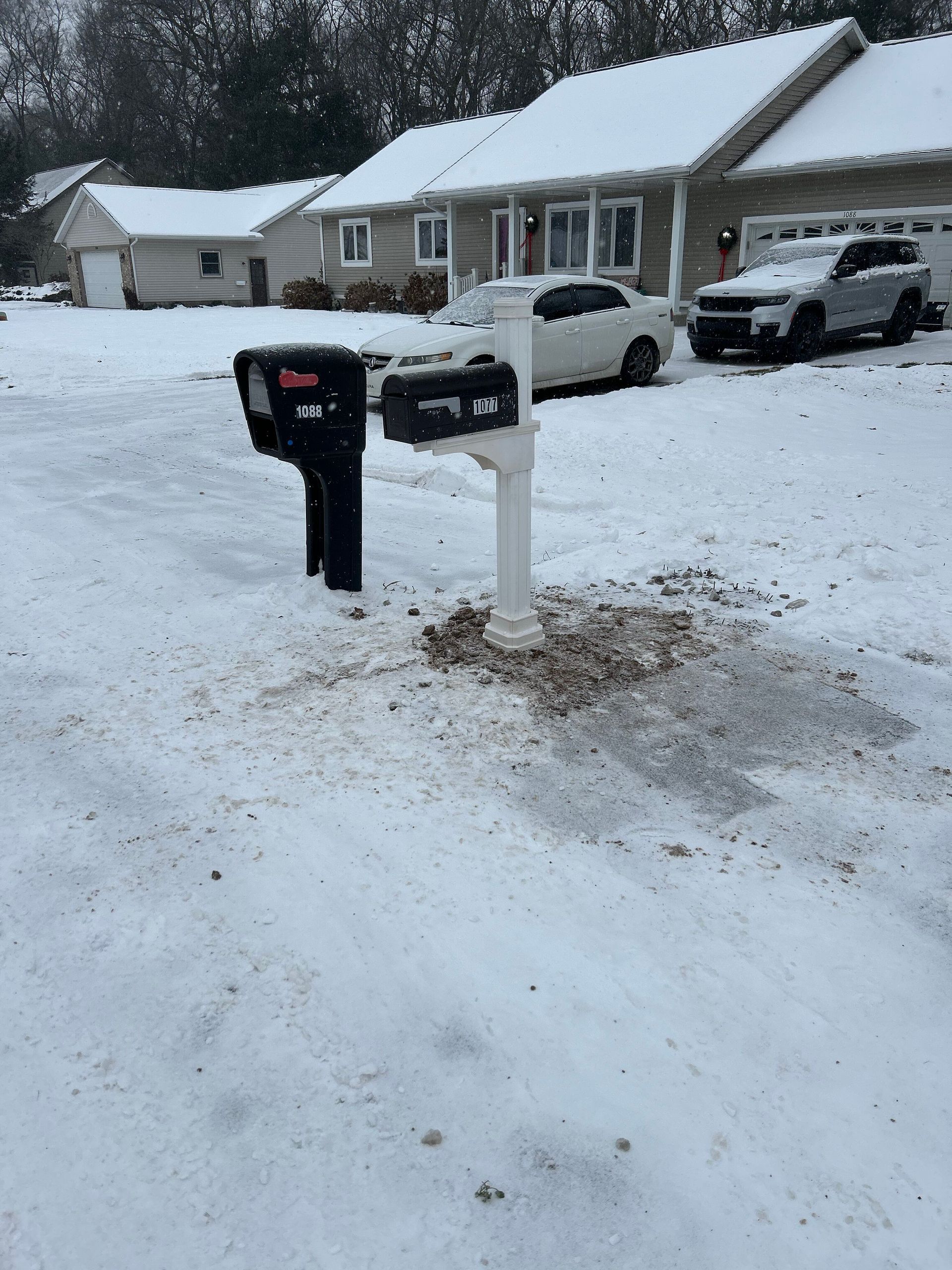 A snowy driveway with a mailbox and cars parked in front of a house
