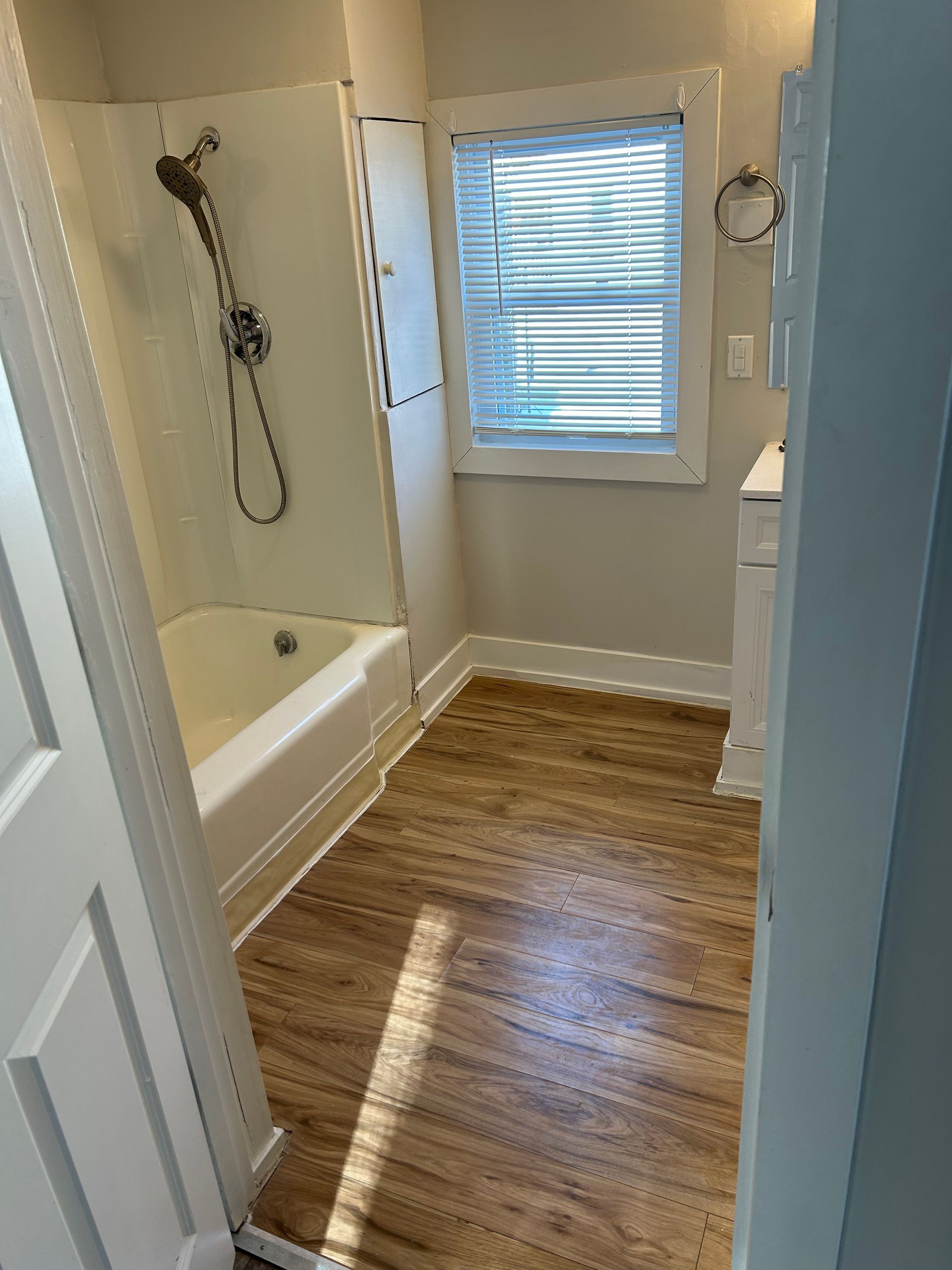 A bathroom with a tub , shower , sink and window.