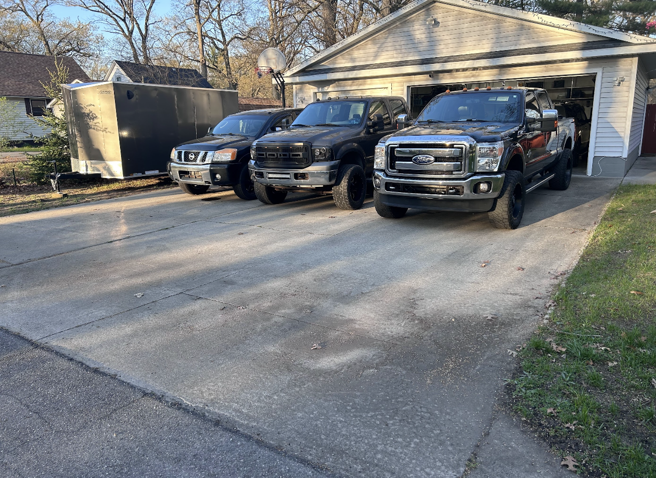 Three trucks are parked in a driveway in front of a garage.