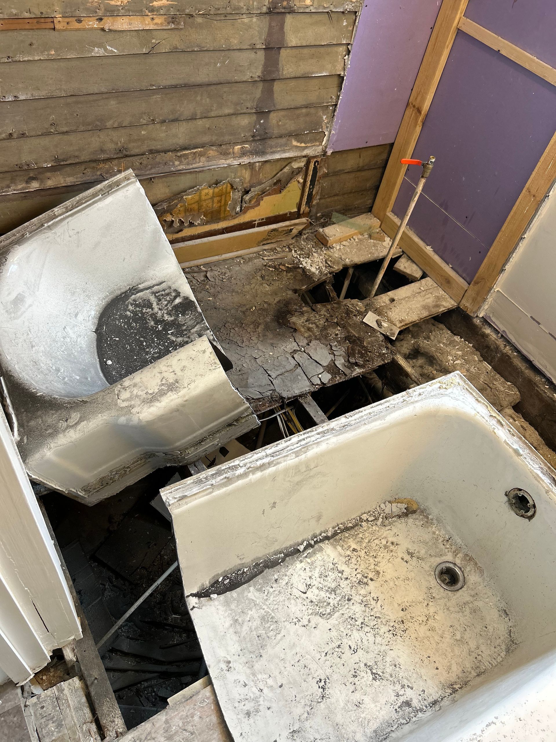 A bathroom with a broken bathtub and a hole in the floor