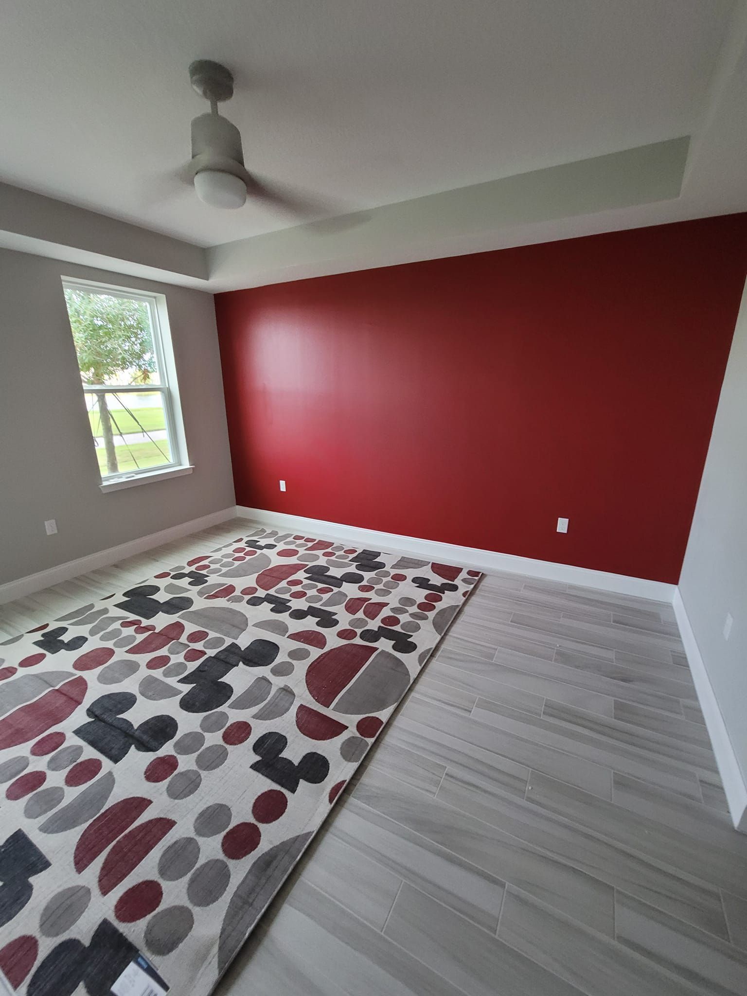 A bedroom with red walls and a rug and a ceiling fan.