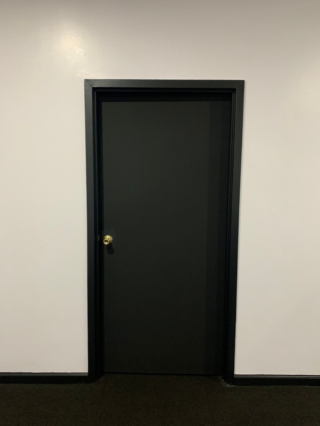 A black door is sitting in a hallway next to a white wall.