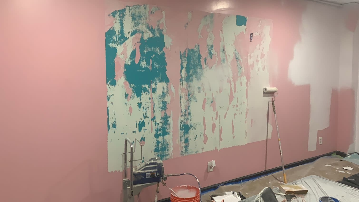 A room with pink walls and white paint being applied to them.