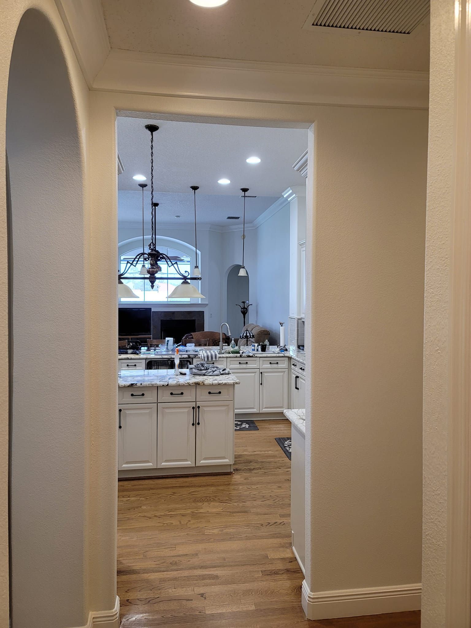 A hallway leading to a kitchen with white cabinets and hardwood floors.