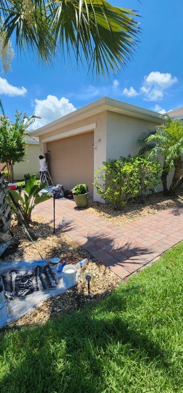 A man is painting the side of a house on a sunny day.