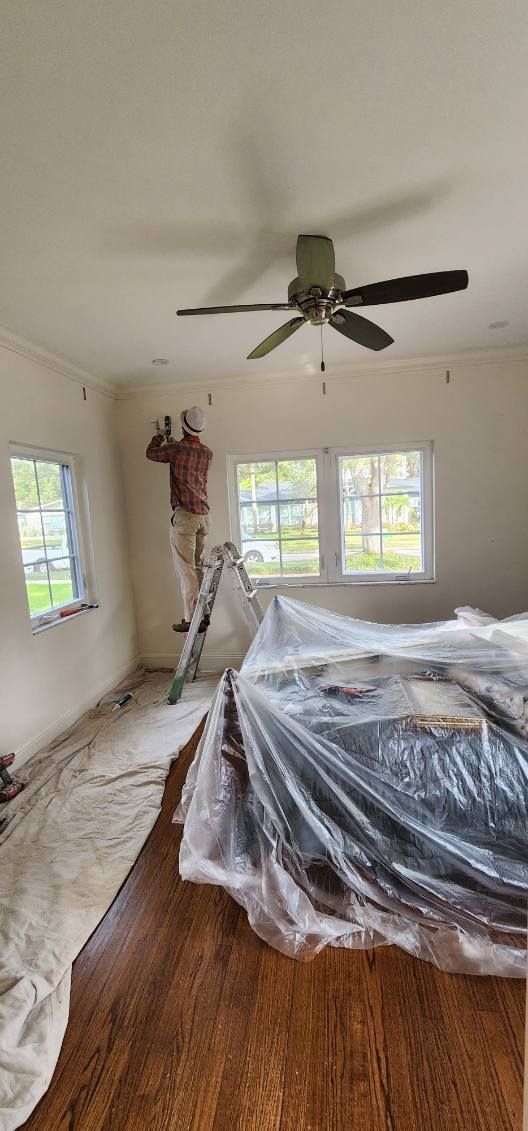 A man is painting the ceiling of a room with a ceiling fan.