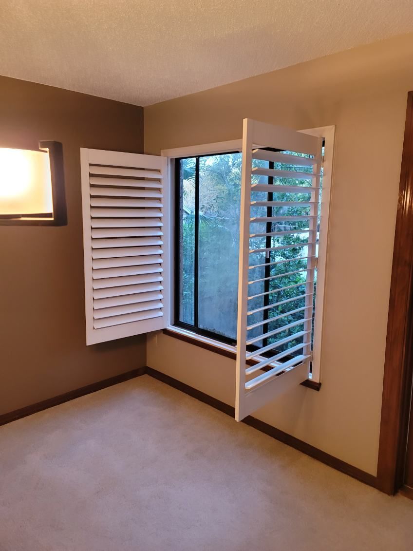 An empty room with a window and shutters open.