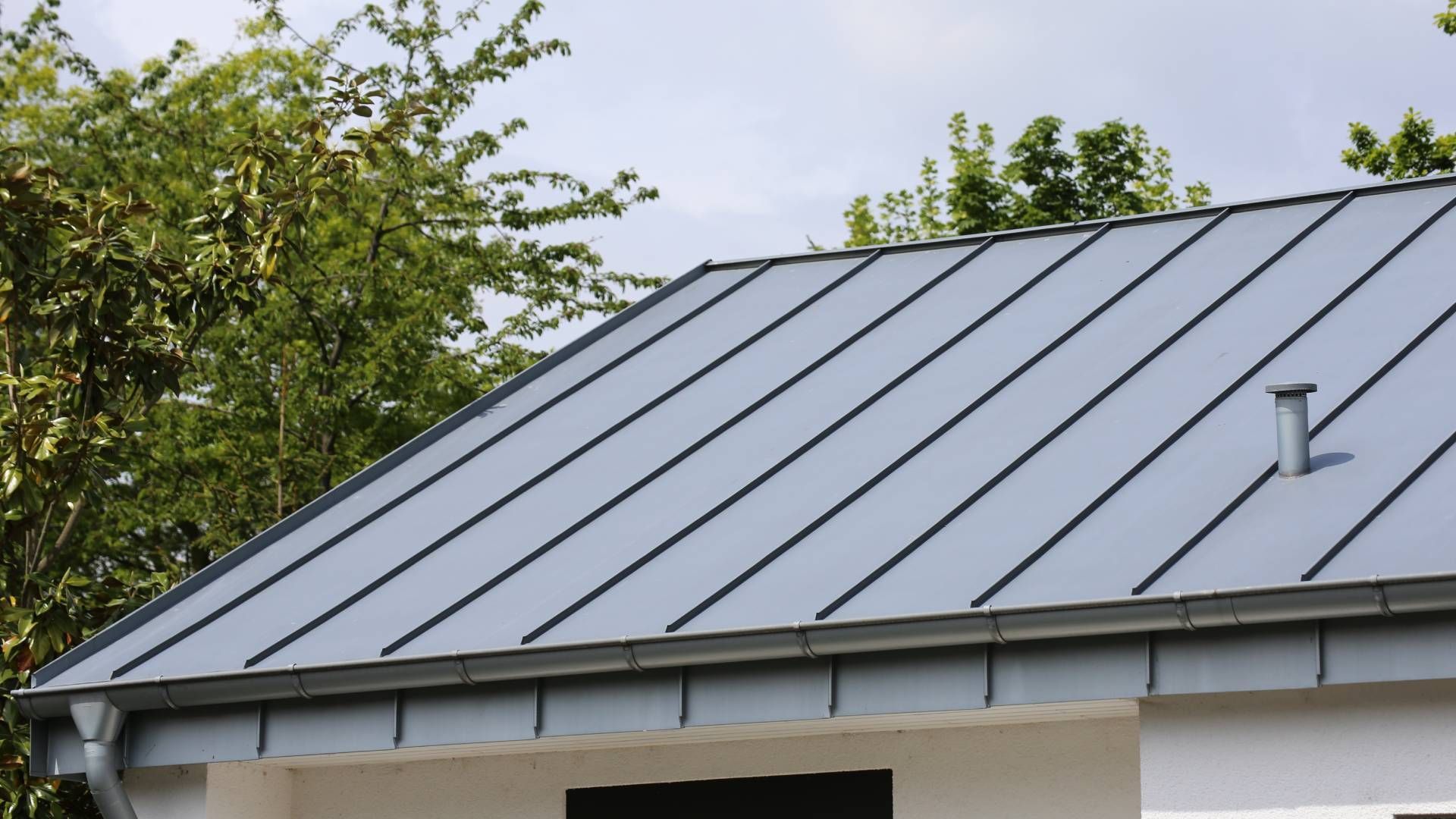 A close up of a roof with a gutter and trees in the background