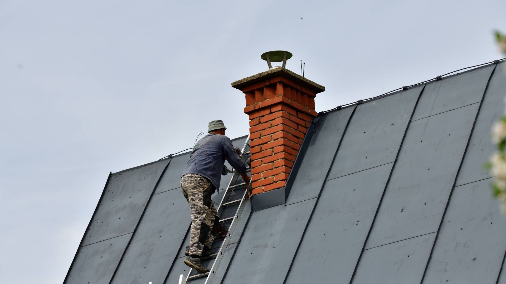 A man is climbing up a ladder to fix a chimney on a roof.
