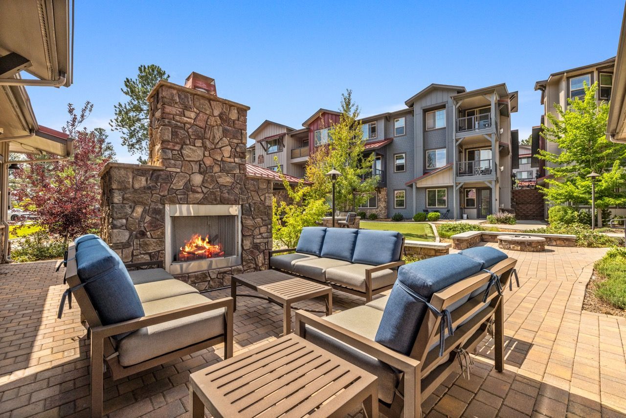 Outdoor community lounge with a stone fireplace, cushioned seating, and a brick patio at Mountain Trail, offering apartments in Flagstaff near NAU.
