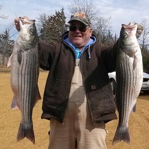 A man in overalls is holding two large fish in his hands