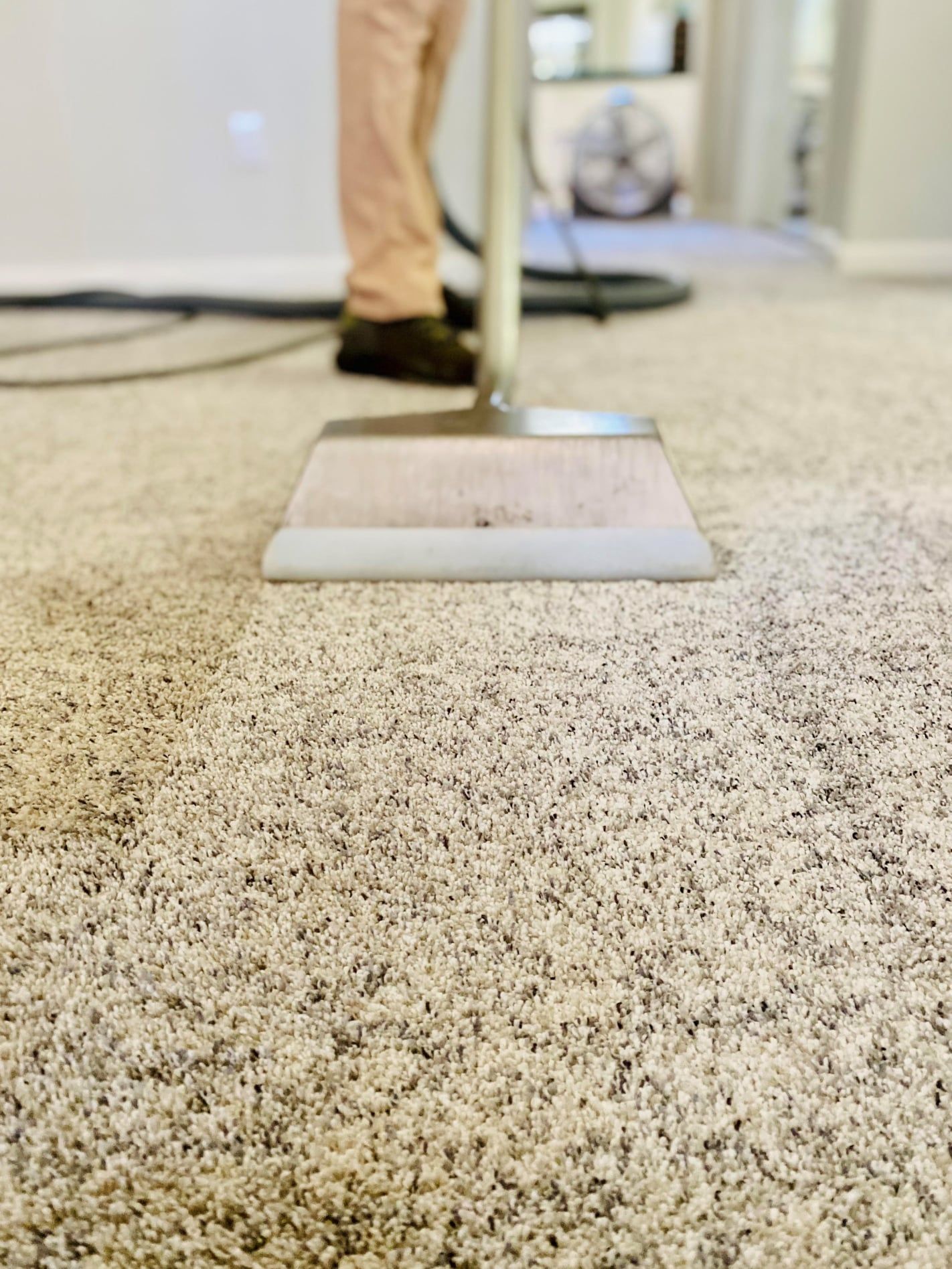 Carpet being cleaned with a machine; person in tan pants and brown shoes.